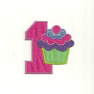 Puede incluir: Número uno de fieltro rosa con una magdalena rosa, morada y verde con un remolino azul y rosa en la parte superior.