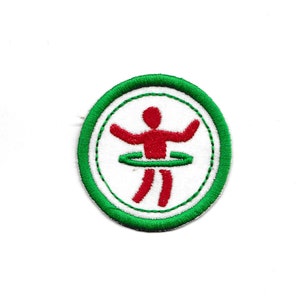 Op de afbeelding: Een geborduurde patch met een groene en witte rand, met een rode stokfiguur die een groene hoelahoep vasthoudt.