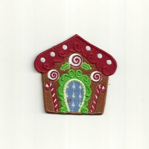 Op de afbeelding: Geborduurde gingerbread house patch met een rood dak, witte stippen, groene snoepstokken en een blauwe deur met witte sneeuwvlokken.