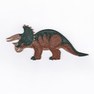 Può includere: Un toppa ricamata di un dinosauro triceratopo, in marrone e verde.