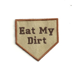 May include: A tan-colored patch with a brown stitched border in the shape of a home plate. The patch has the text "Eat My Dirt" embroidered in brown thread.