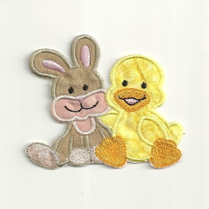 May include: A brown bunny and a yellow duck sitting side by side. The bunny has pink ears and a pink nose. The duck has a yellow beak and orange feet.