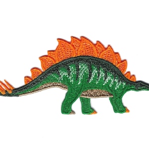 Può includere: Toppa ricamata di dinosauro verde e arancione. Il dinosauro ha una lunga coda e una fila di punte arancioni sulla schiena.