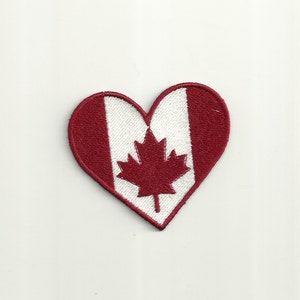 May include: Red heart-shaped patch with the Canadian flag design. The flag features a white field with a red maple leaf in the center and a red vertical stripe on each side.