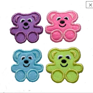 Op de afbeelding: Vier geborduurde strijkpatches van teddyberen in verschillende kleuren: paars, roze, blauw en groen. Elke beer heeft een glimlachend gezicht met zwarte ogen en een zwarte neus.