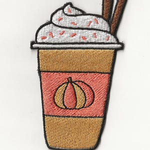 Könnte beinhalten: Gestickter Aufnäher mit einem Pumpkin Spice Latte-Design. Der Aufnäher zeigt einen Kaffeebecher mit Schlagsahne, Streuseln und Zimtstangen. Auf der Vorderseite des Bechers ist ein Kürbis gestickt. Der Aufnäher hat einen schwarzen Rand.