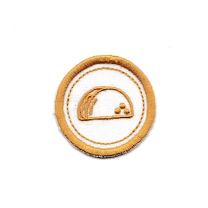 May include: A gold embroidered patch with a white background. The patch features a stylized image of a taco.