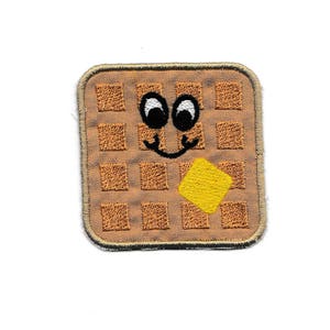 May include: A brown waffle embroidered patch with a smiling face and a yellow pat of butter.