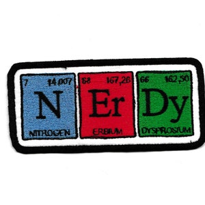 May include: A colourful patch with three squares, each representing a different element from the periodic table. The first square is blue and says "N Nitrogen", the second square is red and says "Er Erbium", and the third square is green and says "Dy Dysprosium".