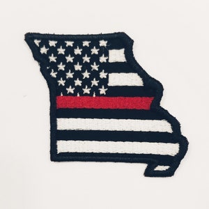以下が含まれることがあります： ミズーリ州の形をした刺繍パッチ。アメリカ国旗にインスパイアされたデザインです。上部は、紺色の背景に白い星があり、その下に白と紺色のストライプが交互に配置されています。中央には赤いストライプが水平に走っています。