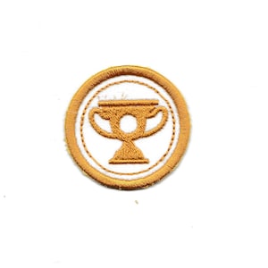 May include: A gold embroidered patch with a white outline depicting a trophy cup.