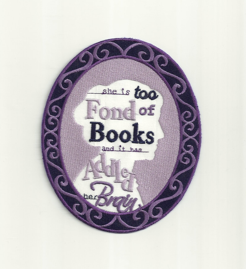 May include: Purple and white embroidered patch featuring a silhouette of a woman's head within an oval frame. The text reads "She is too fond of books and it has added to her brain."