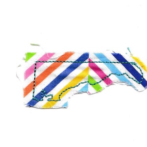May include: A colorful fabric patch in the shape of the state of North Carolina. The fabric is striped with diagonal lines of blue, green, yellow, orange, pink, and white. The outline of the state is stitched in teal thread.