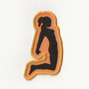 Può includere: Toppa ricamata raffigurante una silhouette nera di una persona seduta. La figura è posta su uno sfondo color pesca, incorniciata da un bordo dorato e arancione. La toppa è destinata a vestiti o accessori.