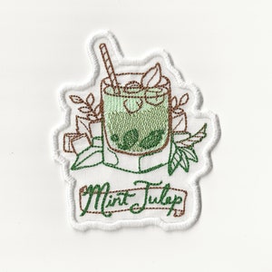 Puede incluir: Parche bordado con un cóctel de julepe de menta verde en un vaso con una pajita marrón y hojas verdes. El texto "Mint Julep" está escrito en una pancarta marrón.