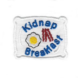 May include: White embroidered patch with blue text that reads "Kidnap Breakfast" and features a red and white illustration of bacon and a fried egg.