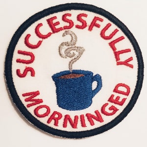 May include: A white embroidered patch with a red circle around the edge. The circle contains the text "Successfully Morned" in red with a blue coffee mug with steam coming out of it in the center.