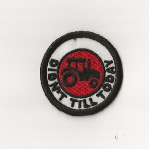 May include: A black and white embroidered patch with a red circle in the center. The circle has a black silhouette of a tractor. The text around the circle reads "Didn't Till Today".