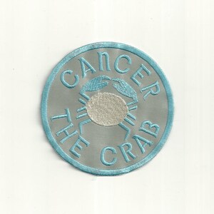 May include: A blue and silver embroidered patch with the text "Cancer The Crab" and a white embroidered crab.