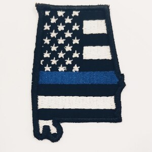 Peut inclure: Un patch de drapeau américain noir et blanc en forme de l'état d'Alabama avec une bande bleue au milieu.