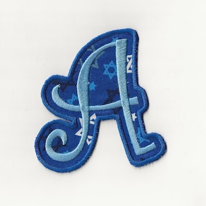 May include: Blue fabric letter A with a white Star of David pattern. The letter is in a cursive font.