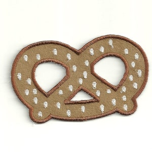 May include: A brown embroidered pretzel with white dots, a popular German baked good.