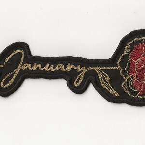 May include: Black embroidered patch with the word "January" in gold thread and a red carnation.