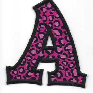 May include: Pink letter A with a black leopard print pattern. The letter is outlined in black and has a slightly raised, puffy texture.