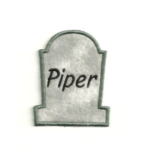 May include: A gray felt tombstone with a green border and the name "Piper" embroidered in black.