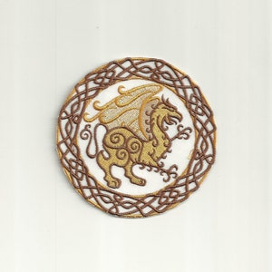May include: A round embroidered patch with a brown Celtic knot border and a gold winged lion in the center.