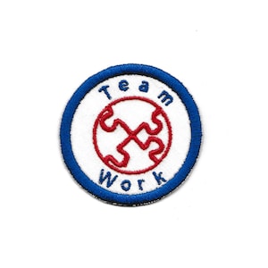 Puede incluir: Un círculo blanco con un borde azul y las palabras "Team Work" en letras azules. Dentro del círculo hay un diseño de pieza de rompecabezas roja entrelazada.