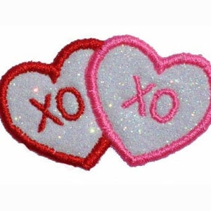 May include: Two white felt hearts with red and pink outlines, each with the letters "XO" in a cursive font.