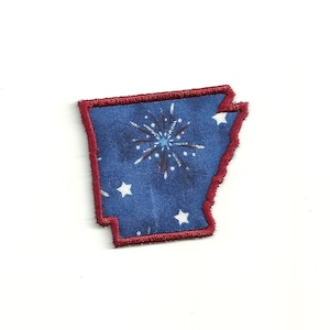 May include: A blue fabric patch in the shape of the state of Arkansas with a red border. The patch has white stars and a firework design in the center.