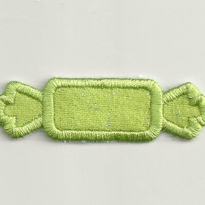 Puede incluir: Un parche bordado en forma de caramelo de color verde claro con un espacio rectangular en el centro para personalizar.