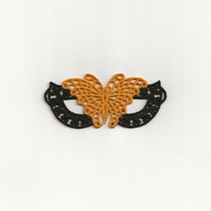 Könnte beinhalten: Eine schwarze Spitzen-Schmetterlingsmaske mit orangefarbenen Akzenten. Die Maske ist zart und filigran, mit einem femininen Design.