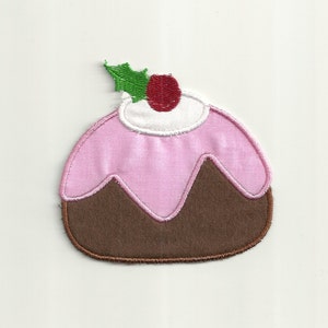May include: A brown and pink felt Christmas pudding with a white icing swirl and a red and green holly sprig on top.