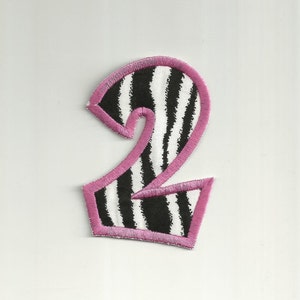 May include: A pink and white striped fabric number two with pink stitching around the edges.