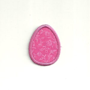 May include: Pink fabric Easter egg with a white floral pattern and a pink stitched border.