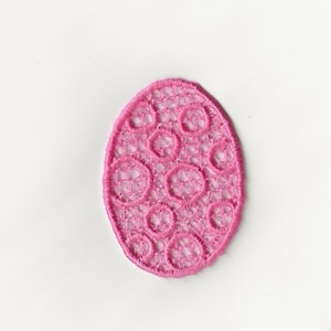 May include: Pink lace applique in the shape of an egg. The lace has a delicate, intricate design with small circles.