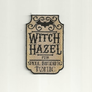 Könnte beinhalten: Ein beigefarbener Stoff-Patch mit schwarzer Stickerei. Der Patch zeigt eine Fledermaus, die Worte "Witch Hazel", "For Spell Binding Tonic" und dekorative Schnörkel.