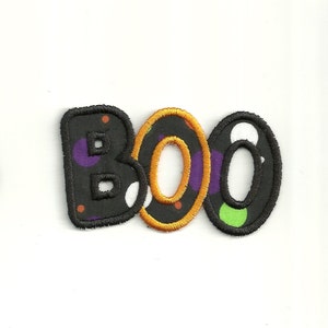 May include: A black fabric patch with the word "BOO" in white letters with colourful polka dots. The letters are outlined in black and the "O"s are outlined in orange.