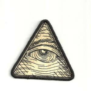 May include: A black and white embroidered patch of an eye inside a triangle. The eye is detailed with lines and a pupil.