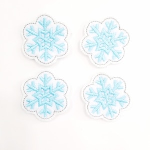 May include: Four blue snowflake embroidery patches with white outlines. The snowflakes are on a white background.
