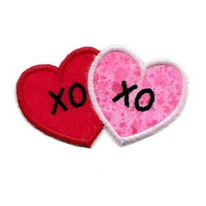 May include: Two felt hearts, one red and one pink, with white stitching around the edges. Both hearts have the letters "XO" embroidered in black.