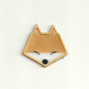 Op de afbeelding: Een bruin geborduurd pleister met het gezicht van een vos met witte ogen en een zwarte neus.