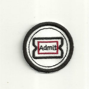 May include: A white fabric patch with a black border and a red rectangle inside. The rectangle has the word "Admit" written in black.