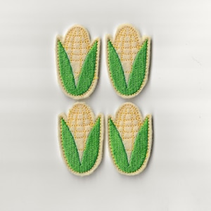 May include: Four embroidered felt patches shaped like ears of corn. Each patch is cream coloured with a yellow corn cob and green leaves.