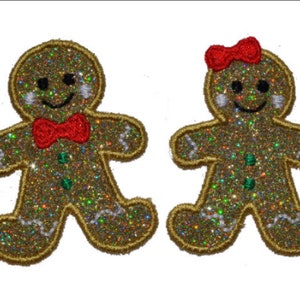 May include: Two gingerbread people, one with a red bow tie and the other with a red bow, are made of sparkly gold fabric.