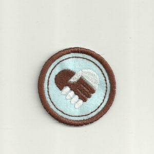 May include: A brown and white embroidered patch featuring a heart shape formed by two hands clasped together. The patch is on a light blue background and has a brown border.