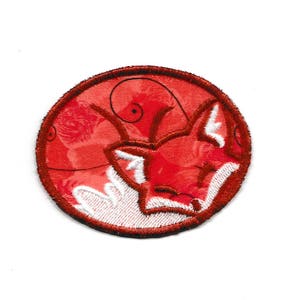 Op de afbeelding: Geborduurde patch met een slapende rode vos op een rode achtergrond met bloemmotieven. Het gezicht van de vos is wit en de patch heeft een donkerrode rand. Geschikt voor kleding of accessoires.